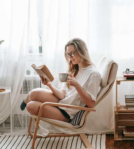 Frau sitzt mit Buch und Kaffee lesend im Sessel